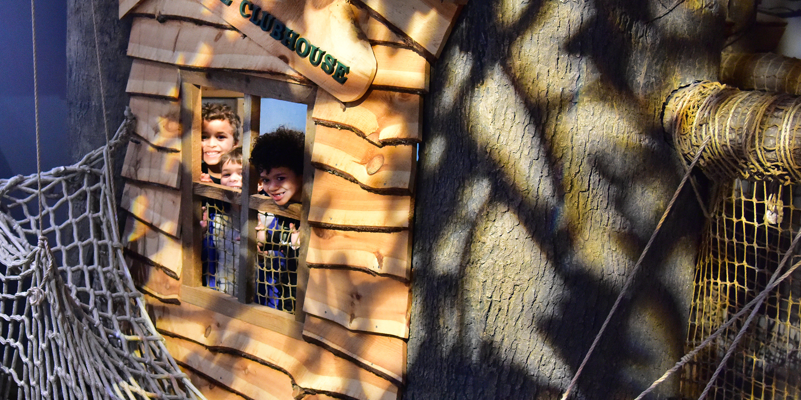 Young children peaking out window of toy wooden treehouse
