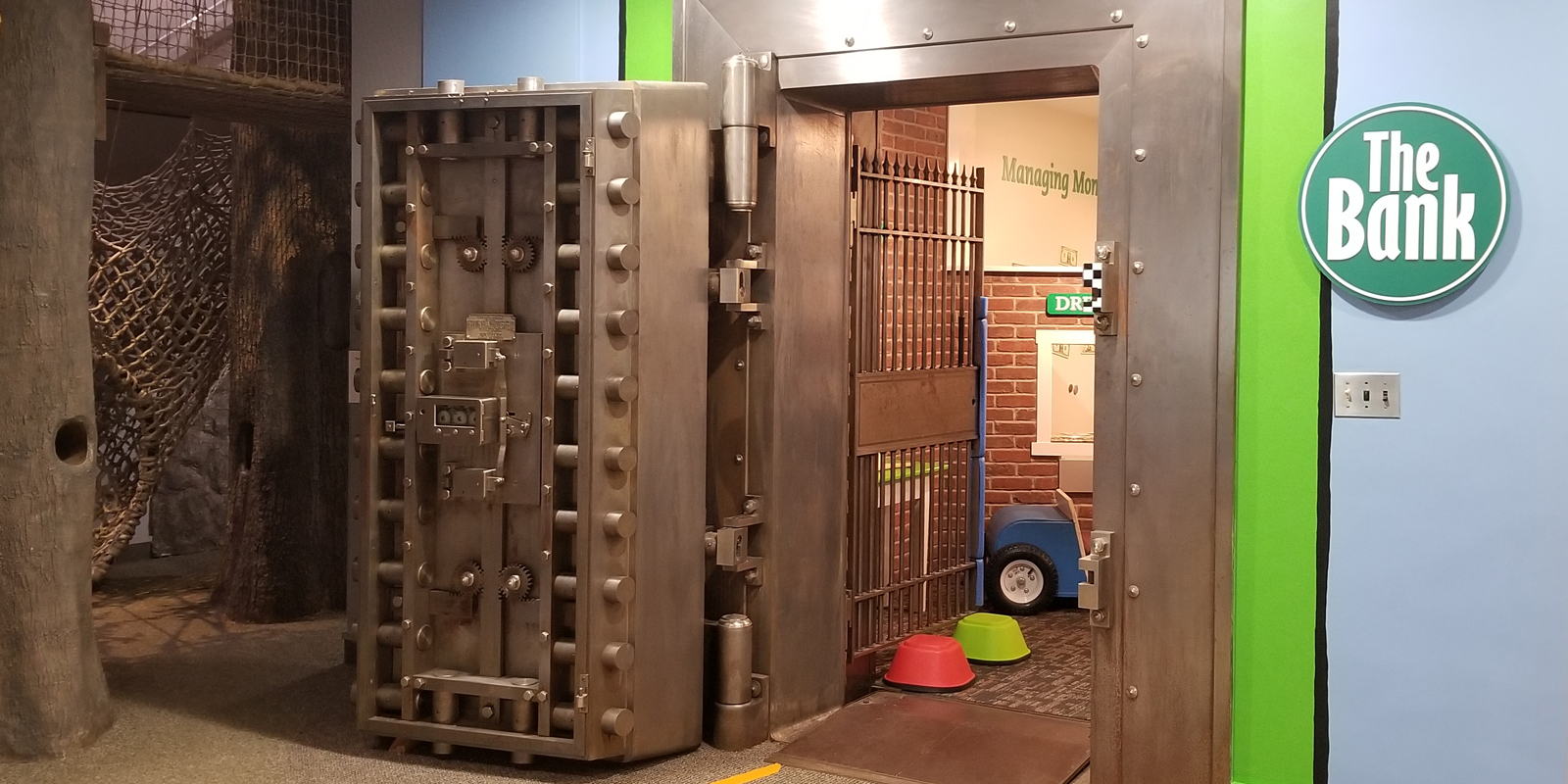 Exhibit of bank vault with green trim and a heavy looking vault door open.
