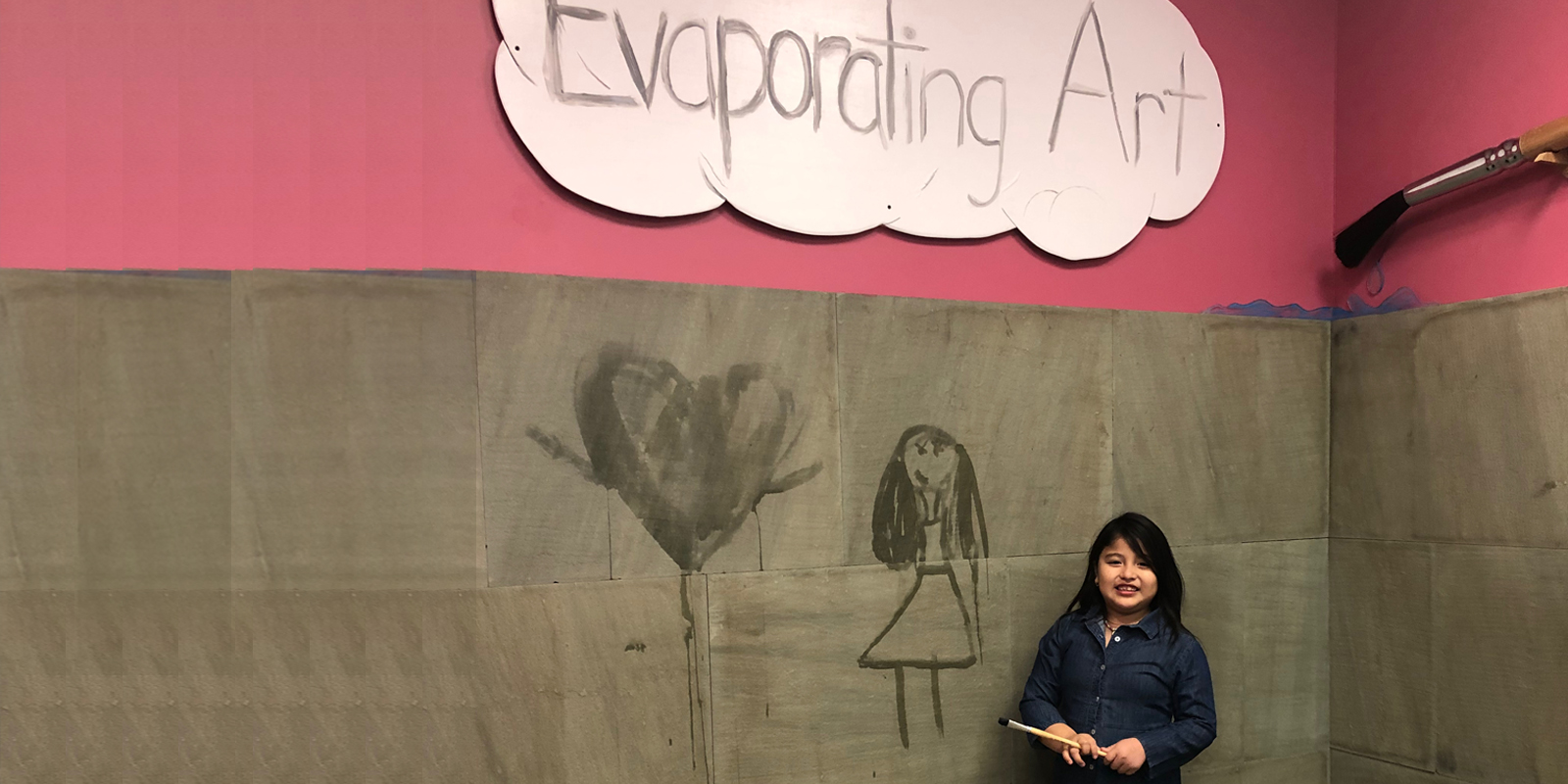Young girl with dark hair and denim dress holding paintbrush below sign that says Evaporating Art