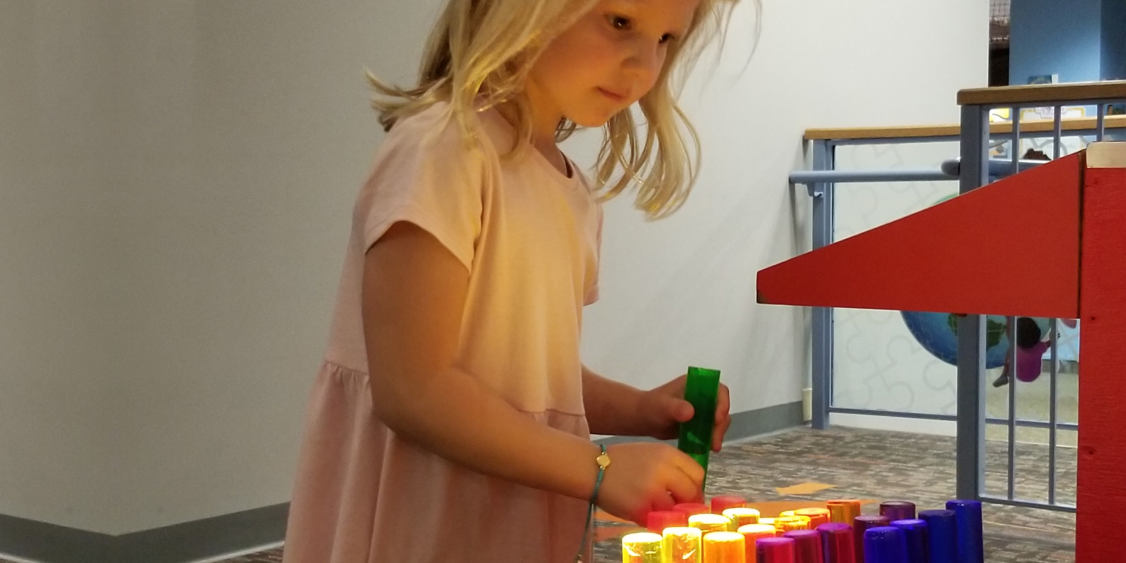 Young girl with blonde hair and pink dress playing with an oversized light bright toy with colorful pegs