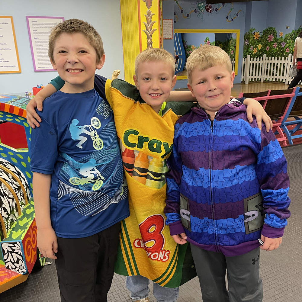 Three boys arm in arm with middle boy wearing a crayon box costume