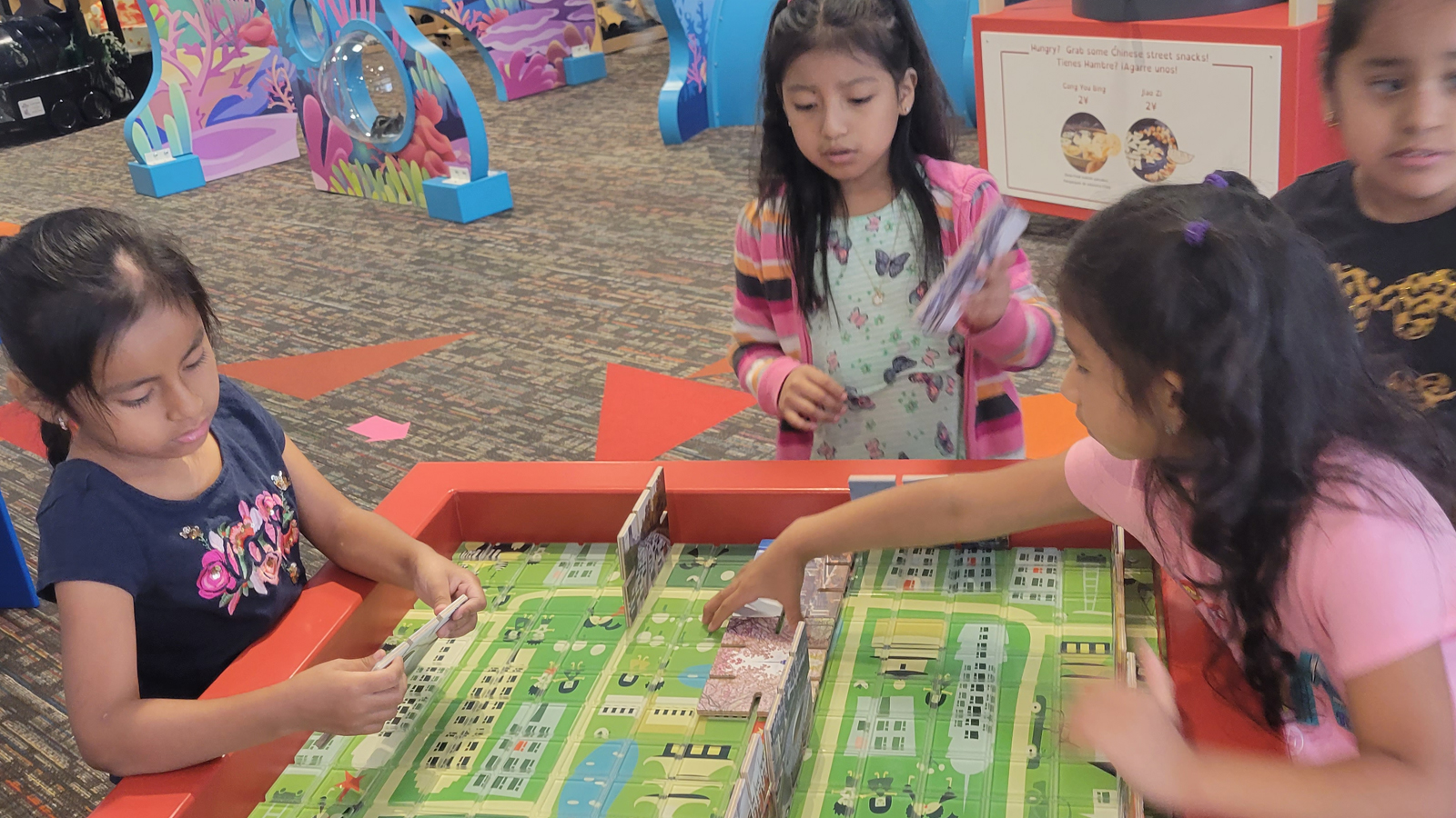 Four young girls playing at a table with an interactive board game
