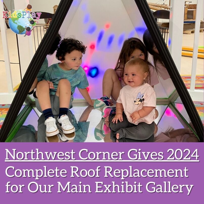 A square graphic announcing KidsPlay's Northwest Corner Give project. The KidsPlay logo is in the upper left hand corner. It is on top of a photo of a young girl, a young boy, and a baby playing in KidsPlay's prototype Giant Kaleidoscope exhibit. Underneath that, white text on a purple background reads "Northwest Corner Gives 2024: Complete Roof Replacement for Our Main Exhibit Gallery."