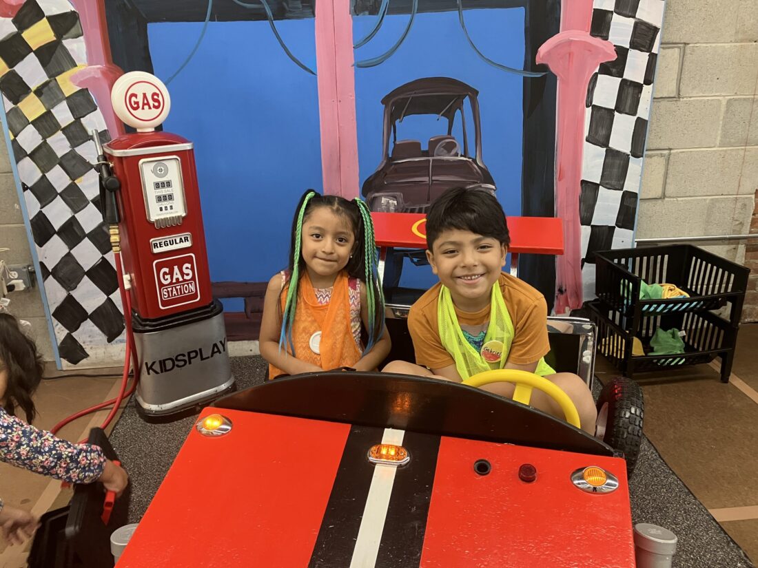 A photo of two children from the KidsPlay Day Camp playing in the KidsPlay Racecar exhibit.