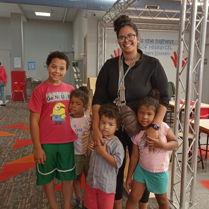 A photo of KidsPlay visitor Nicole and her four children standing in front of the Maker Space exhibit at KidsPlay Children's Museum in Torrington, CT.